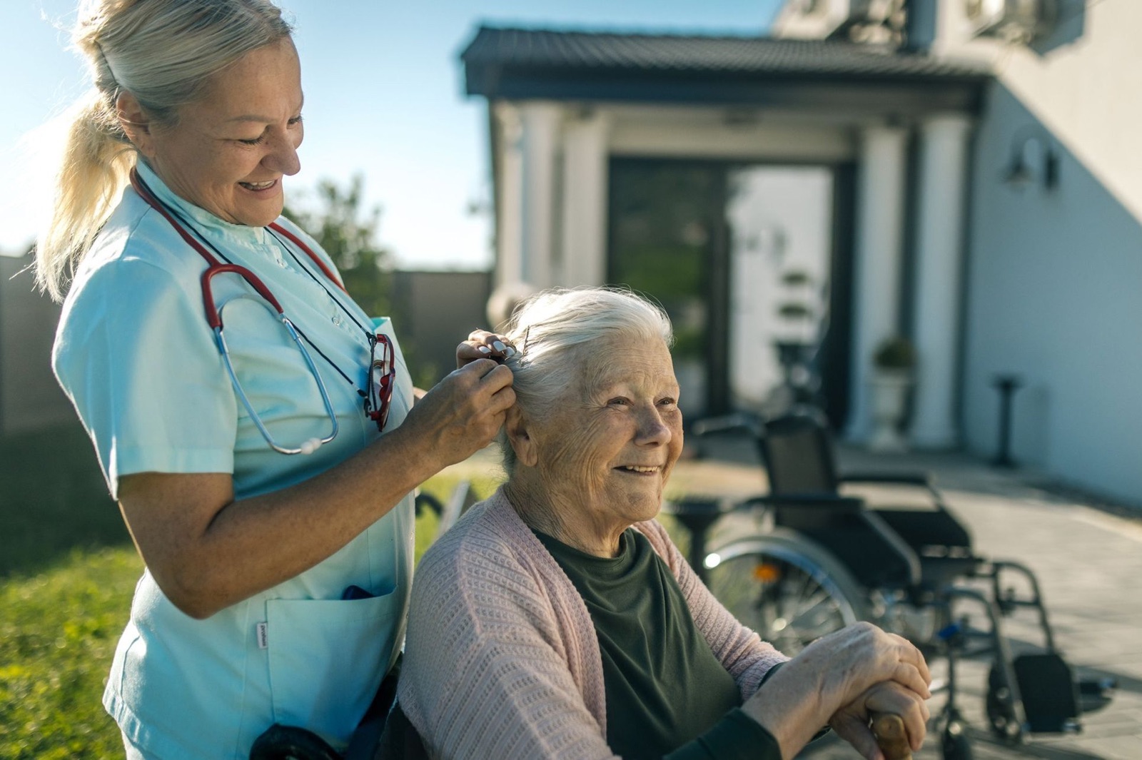Eine Begleiterin richtet einer älteren Frau im Garten liebevoll die Haare